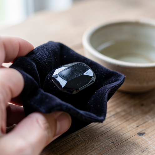 Gros plan réaliste d’une obsidienne noire portée dans une petite pochette en velours, avec une ambiance calme et des éléments de nettoyage comme un bol en céramique sur une table en bois.